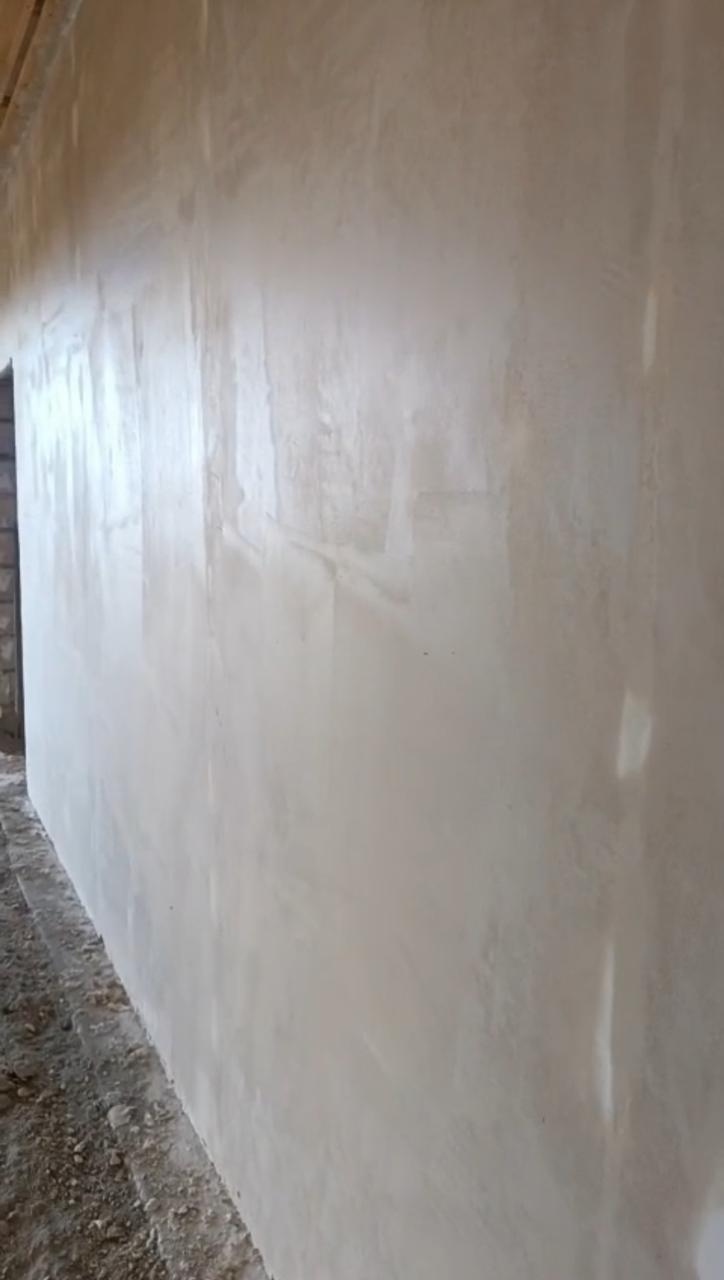 Свежая штукатурка на длинной стене с равномерными следами кельмы и мягким блеском.