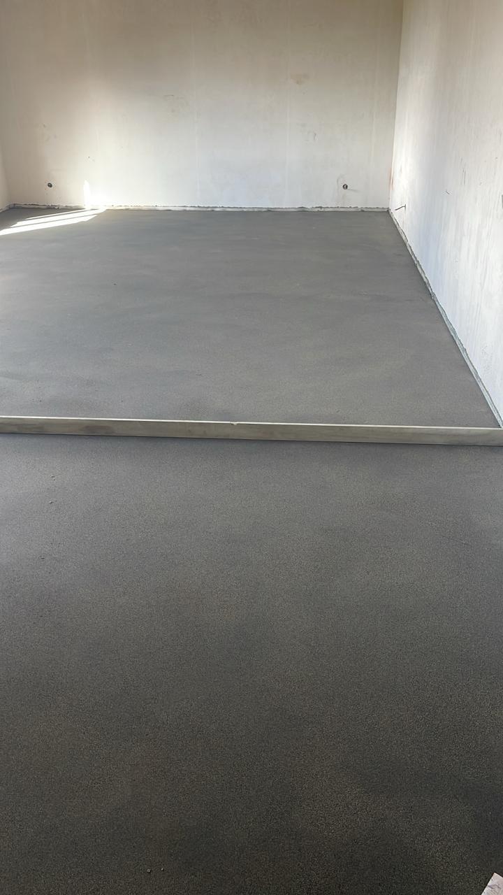 Пустая комната с гладкой тёмно-серой стяжкой и правилом на полу.