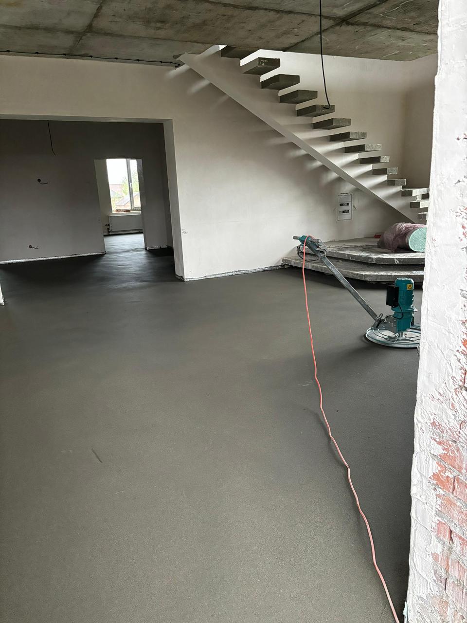 Просторное помещение со стяжкой, затирочной машиной и парящей лестницей.